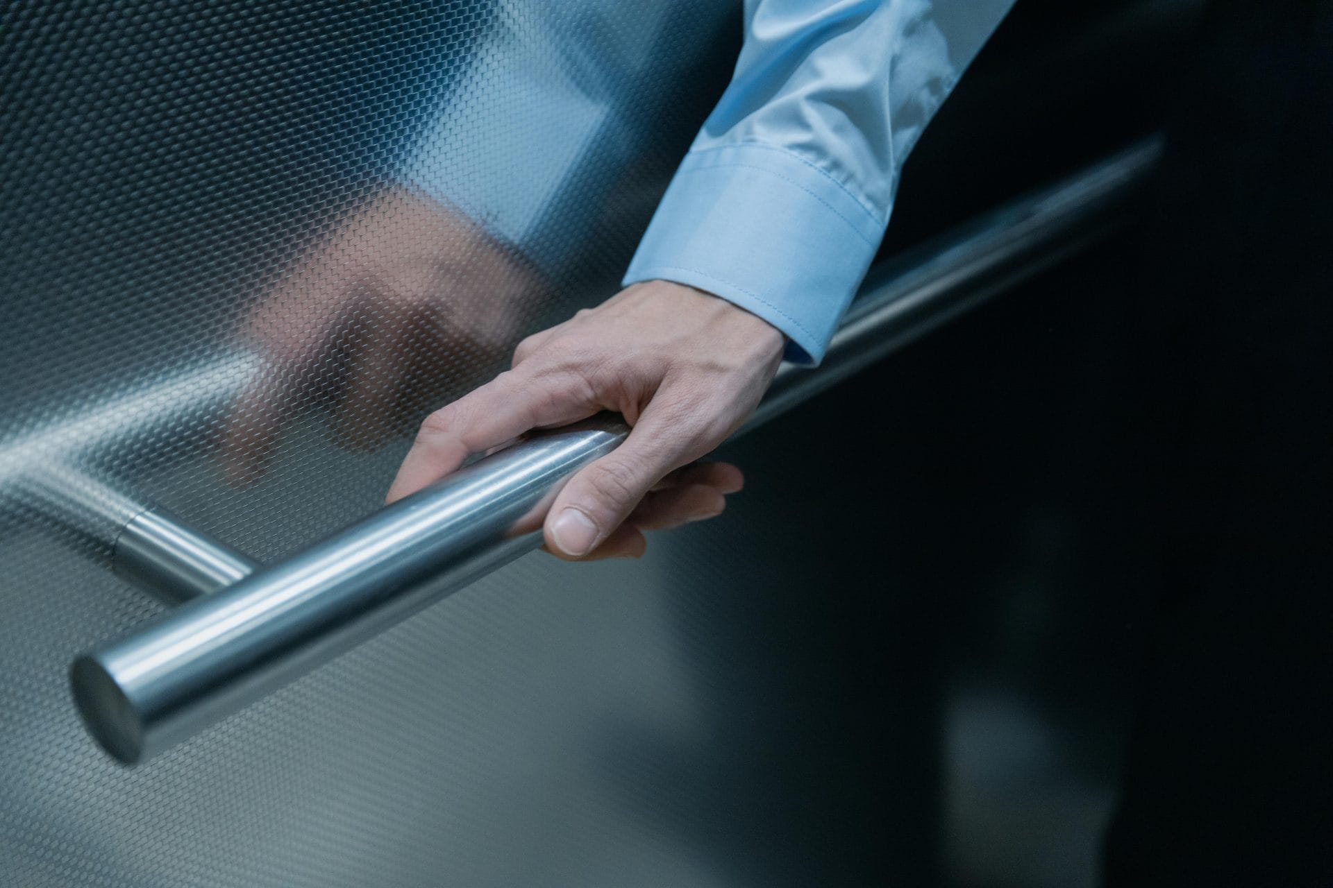 A man holding a handrail inside a passenger lift.